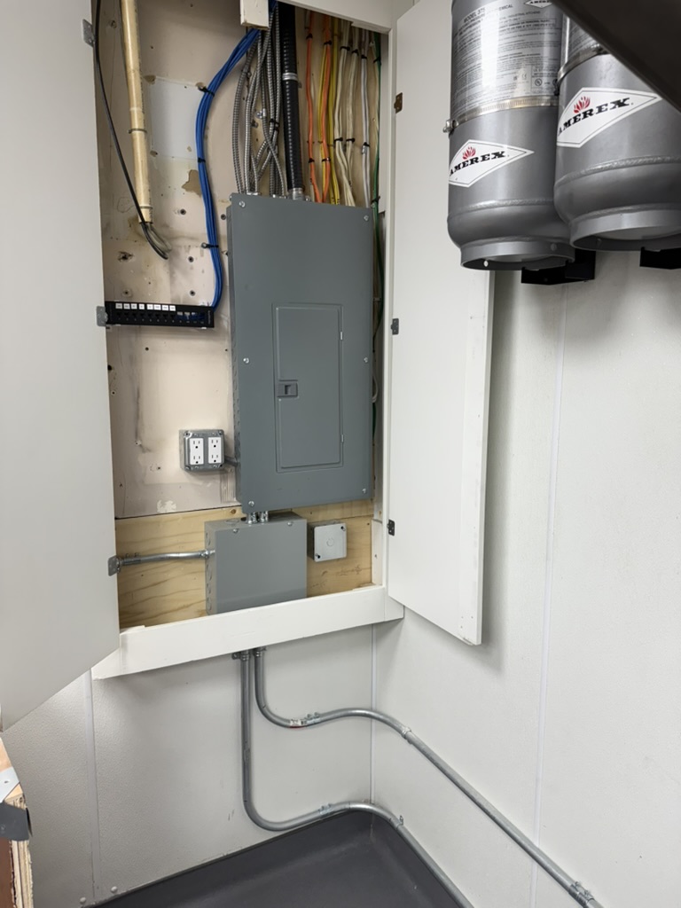 Open electrical panel with wiring and conduits inside a cabinet; two gray Merex canisters mounted on the right.