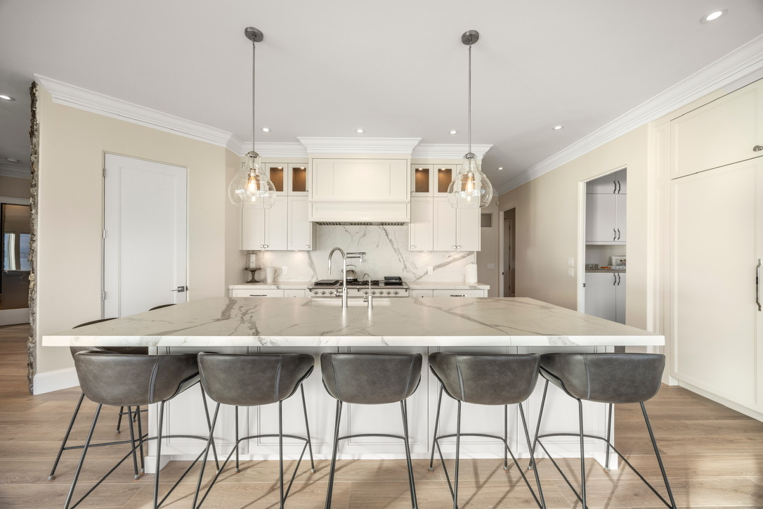 Bright modern kitchen with a large marble island and six gray bar stools along the seating side.