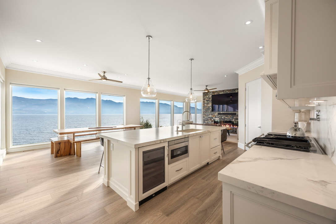 Bright coastal kitchen with a large island, white cabinetry, and ocean view through wide windows.