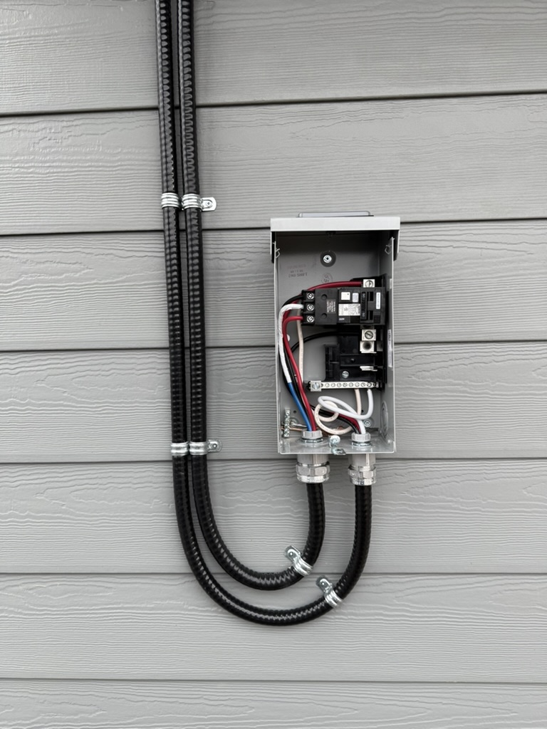 Exterior electrical service panel mounted on siding with red, blue, white wires and conduit running to the building's electrical system