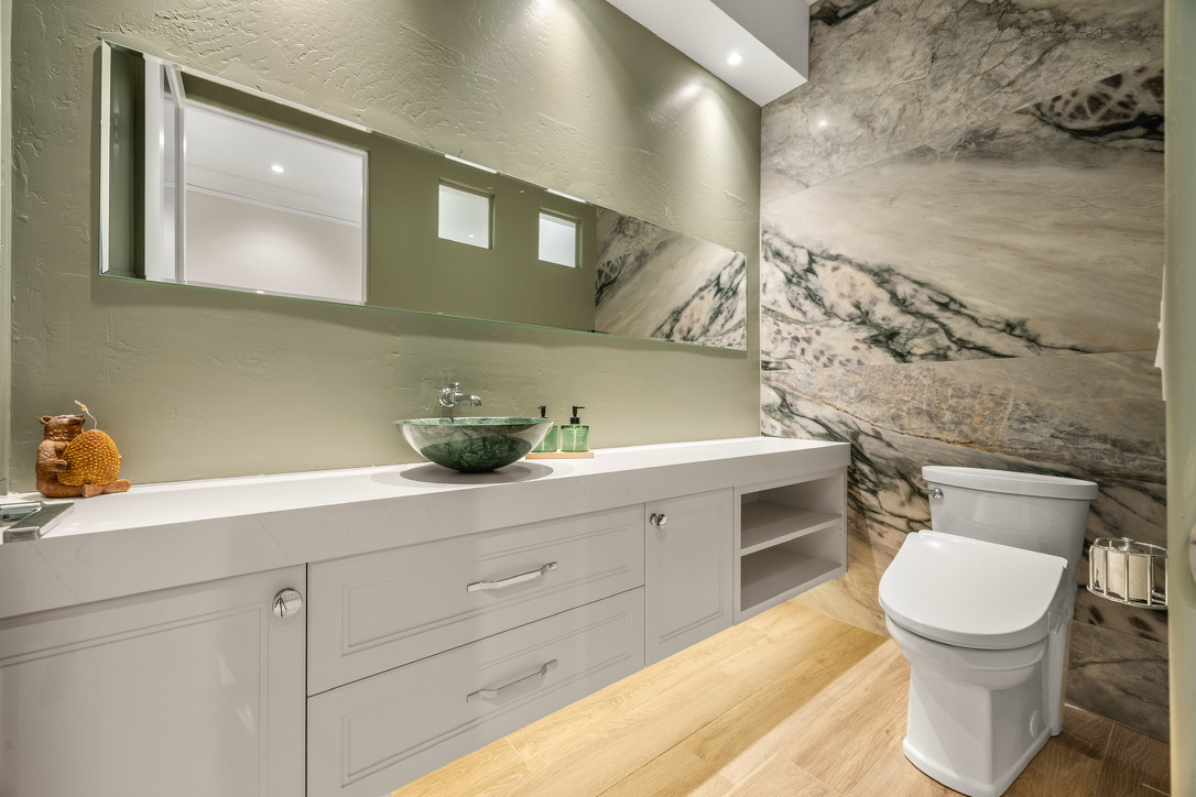 Contemporary bathroom with a green vanity wall, marble accent wall, white cabinetry, and a green stone vessel sink.